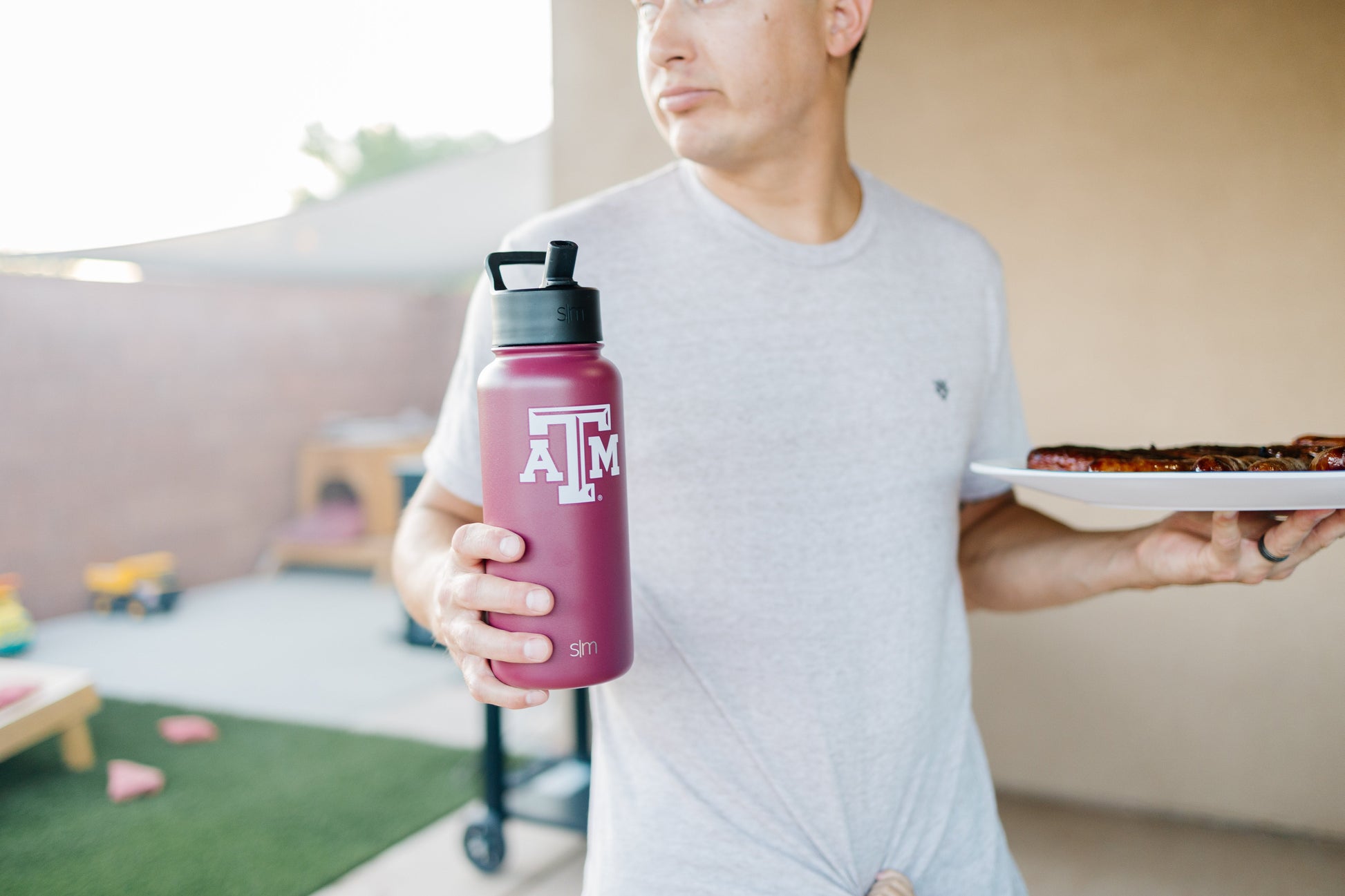 Burgundy water bottle held by man in light gray t-shirt against beige and cream background